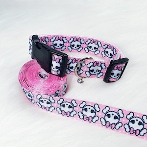 May include: Pink dog collar with a skull and crossbones pattern and a matching lead. The collar has a black buckle and the lead has a pink and white skull and crossbones pattern.