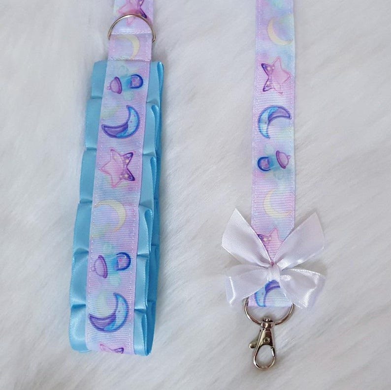 May include: A light blue and white ribbon with a moon and star pattern. The ribbon is attached to a white bow and a silver key chain.