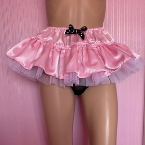Peut inclure: Une jupe en satin rose avec un nœud noir à pois blancs et un volant en tulle blanc.