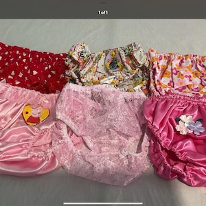 May include: A collection of six pairs of ruffled knickers featuring various designs including a red pair with white hearts, a patterned print, a floral print, a pink satin pair with a Peppa Pig patch, a pink lace pair, and a pink satin pair with flowers.