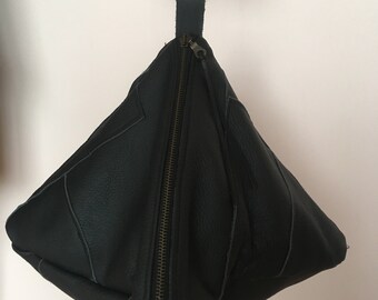 May include: A black leather pyramid-shaped bag with a zipper closure and two metal rings at the top.