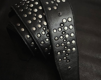 May include: Black leather guitar strap decorated with silver studs. The strap is rolled, displaying the stud pattern. The studs are arranged in a pattern across the strap.