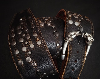 May include: A black leather belt with silver studs and a silver buckle featuring two animal heads. The belt has a distressed look with brown edges and black stones. The belt is a fashion accessory.