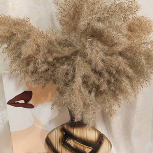 Puede incluir: Un ramo de hierba de la pampa seca en un jarrón de cerámica marrón y negro. El jarrón tiene un acabado texturizado, similar a la madera.