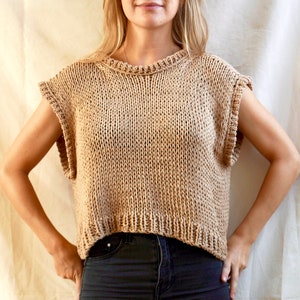 May include: A sleeveless knitted top in a light brown colour. The top has a round neckline and a cropped length.