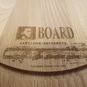 Può includere: Un tagliere in legno con un design inciso a laser che presenta un ritratto del compositore Frédéric Chopin, note musicali e il testo "BOARD FANTASIE - IMPROMPTU.  Franciszek Chopin 1810-1845".