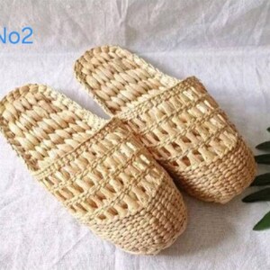 May include: A pair of woven beige slippers. The slippers are made of a natural fiber with an open weave design. The text "No2" is in the upper left corner. The slippers are on a white surface.