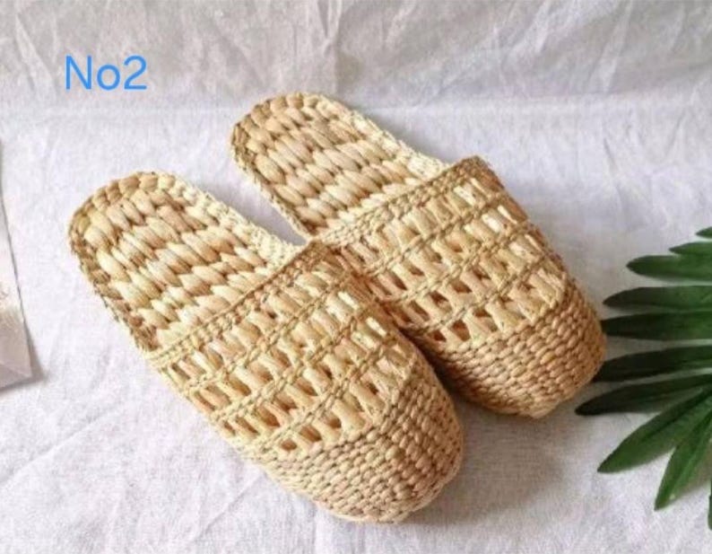 May include: A pair of woven beige slippers. The slippers are made of a natural fiber with an open weave design. The text "No2" is in the upper left corner. The slippers are on a white surface.
