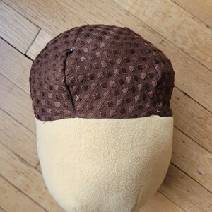 May include: A plush acorn-shaped cushion with a brown, textured top and a light yellow, smooth bottom. The cushion is designed to resemble a real acorn, with a rounded shape and contrasting colours.