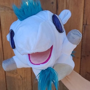 May include: A white plush unicorn hand puppet featuring a gold horn, bright blue faux fur mane and tail, large dark blue oval eyes, and a pink open mouth. The puppet has grey fabric hooves on its limbs and a soft, white plush body texture.