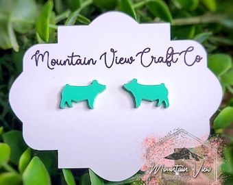 May include: A pair of teal blue pig silhouette earrings on a white card with the text "Mountain View Craft Co."