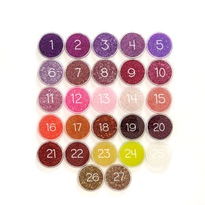 May include: Twenty-seven small jars of glitter, each with a number from 1 to 27. The glitter is in various colors, including purple, pink, red, orange, and gold.