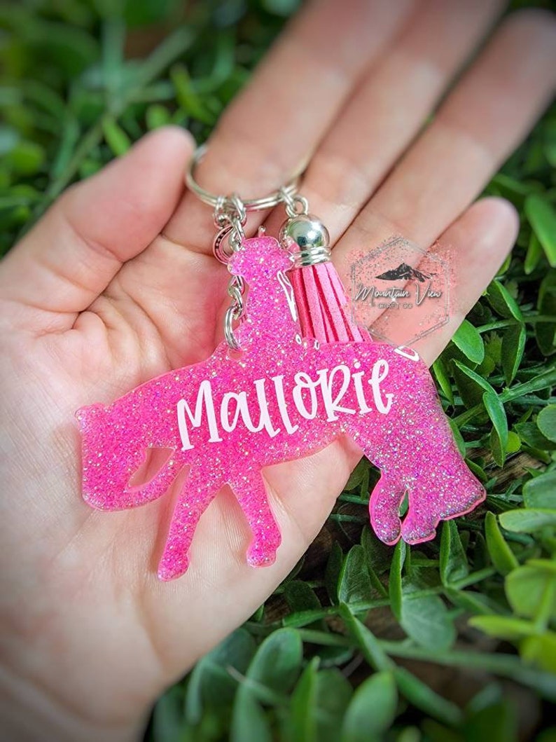 May include: Pink glitter horse keychain with a pink tassel and the name "Mallorie" written in white.