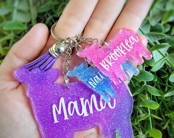 May include: Purple, pink, and blue glitter cow keychain with the words "Mama", "Nat", and "Brooklea" on each cow.