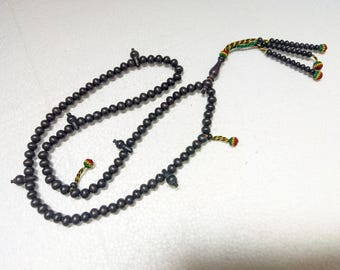 May include: A string of dark brown prayer beads featuring small, round wooden beads arranged in a loop. The strand includes several decorative dividers and is finished with a braided cord in red, yellow, and green, ending in three small tassels.
