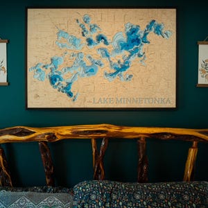 May include: A wooden bed frame with a rustic design is the focal point of the room. Above the bed, a framed map of Lake Minnetonka with blue water details hangs on a teal wall. Two framed botanical prints are also displayed.