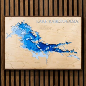 May include: A wooden 3D bathymetric map of Lake Kabetogama featuring layered blue water depths, a light wood frame, and engraved text including St. Louis County, 24,034 Acres, Shore Length 192.54 Miles, Maximum Depth 80 Feet, and Average Water Clarity 8.8 Feet.