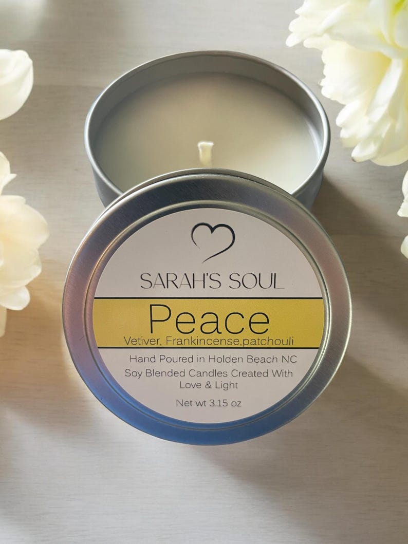 May include: A silver tin candle with a white label that reads "SARAH'S SOUL Peace Vetiver, Frankincense, patchouli Hand Poured in Holden Beach NC Soy Blended Candles Created With Love & Light Net wt 3.15 oz".