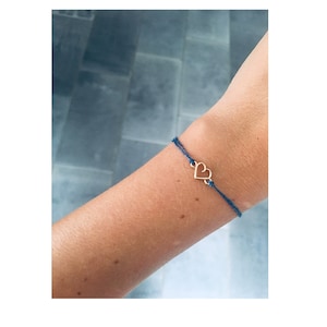 Puede incluir: Un brazalete de cuerda azul con un dije de corazón dorado.