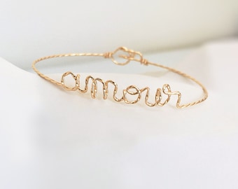 May include: A gold wire bracelet with the word "amour" spelled out in wire.
