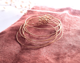 May include: A set of five thin gold-toned wire bangles, each featuring a simple hook-and-eye clasp mechanism. The bracelets are constructed from smooth, circular metal wire and are stacked together to display their uniform, minimalist design.