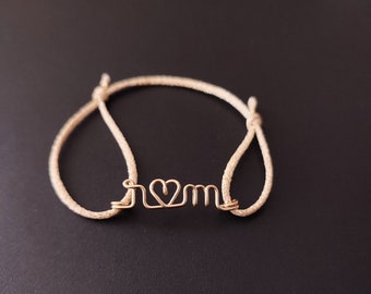 May include: A beige string bracelet with a gold wire charm that says "I love mom".