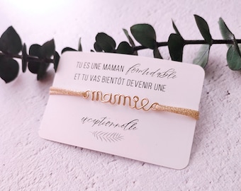 May include: A gold-colored bracelet with the word "mamie" spelled out in wire. The bracelet is on a white card with the text "Tu es une maman formidable et tu vas bientôt devenir une exceptionnelle" in French.