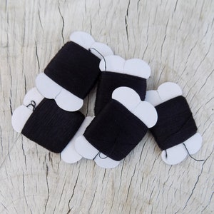 May include: Five spools of black thread wrapped in white paper with scalloped edges.
