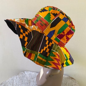May include: A wide-brimmed bucket hat with a colorful African print pattern in shades of yellow, red, green, and black. The hat has a black underside.