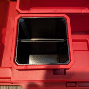 May include: A red plastic tool box with a black insert. The insert is divided into two compartments. The tool box is designed to hold tools and other small items. The image is taken from a top-down perspective.