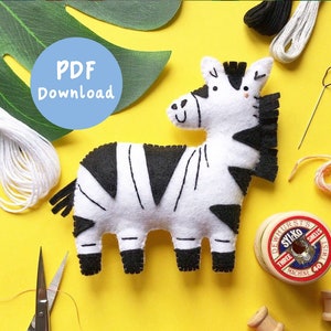 Könnte beinhalten: Ein schwarzes und weißes Filz-Zebra-Spielzeug mit einem lächelnden Gesicht. Das Zebra befindet sich auf einem gelben Hintergrund mit Nähzubehör, darunter Garn, Schere und eine Garnrolle.