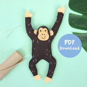 May include: A brown felt monkey with black stitching and pink cheeks, hanging with its arms raised. The monkey is on a light blue background with a roll of brown felt and sewing needles. A blue circle with the text "PDF Download" is in the upper right corner.