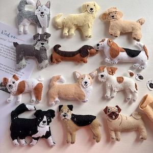 May include: A collection of twelve handcrafted felt dog ornaments in various breeds and colours, including a grey husky, golden retriever, brown dachshund, and black and white border collie, arranged on a surface with an instruction sheet.