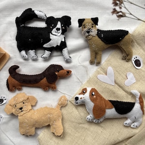 May include: A collection of handmade felt dog figurines in various breeds, including a black and white Border Collie, a tan and black terrier, a brown and tan dachshund, a tan poodle, and a white, brown, and black basset hound.