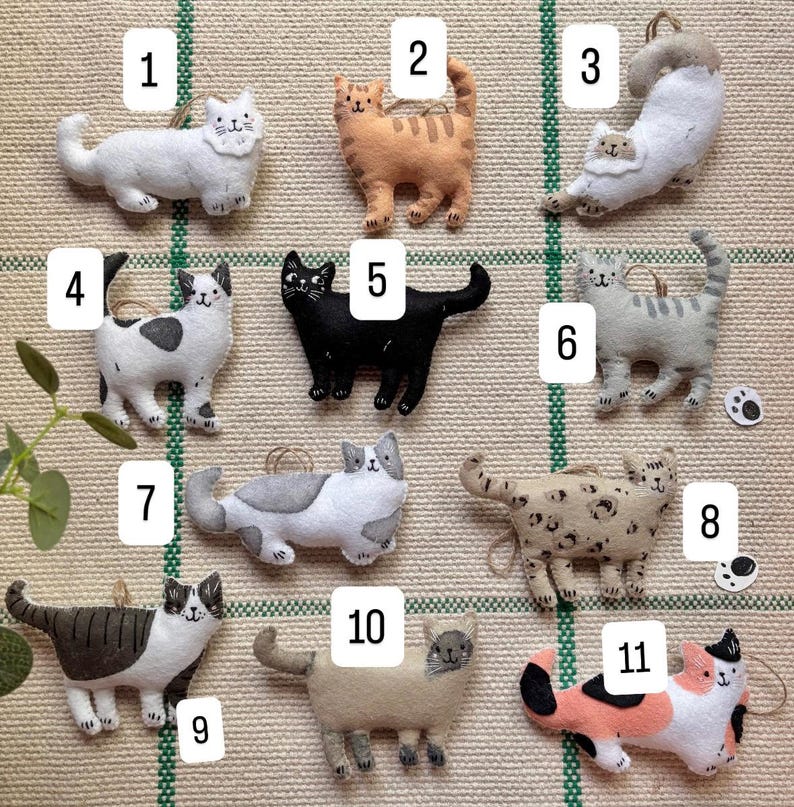 May include: A collection of eleven felt cat ornaments in various colors and patterns. Each cat has a loop for hanging. The cats include white, orange, black, gray, and calico designs. The ornaments are handmade and suitable for cat lovers.