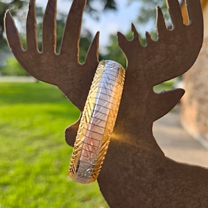 May include: A gold and silver two-tone bangle bracelet with a geometric pattern.