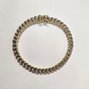 May include: A gold bracelet with a series of small, sparkling stones set in a repeating pattern. The bracelet is closed with a gold clasp. The jewelry is displayed on a white surface.