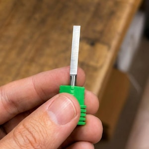 以下が含まれることがあります： 鋭い直線状の刃を持つ平らな長方形の金属製カッターブレード。明るい緑色の円筒形プラスチック製ハンドルに取り付けられており、ハンドルにはリブ状のテクスチャが施されているため、精密な切断や彫刻作業の際に手でしっかりと握って制御することができます。