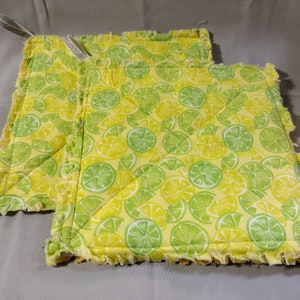 May include: Two yellow and green kitchen pot holders with a lemon and lime print. The pot holders have a frayed edge and are made of fabric.