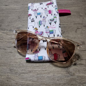 May include: A pair of brown sunglasses with a clear frame and a white and pink llama print fabric case. The case has a pink zipper pull.
