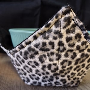 May include: A black and white leopard print fabric bowl cozy. The cozy is made of a soft, quilted fabric and is designed to fit a standard-sized bowl.
