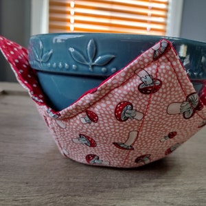 May include: A blue ceramic bowl with a leaf design is nestled inside a pink fabric bowl with a white polka dot pattern and red mushroom illustrations.