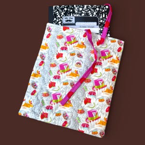 May include: A patterned tote bag with a design of rabbits, teacups, and top hats. The bag has a pink and red strap and holds a composition notebook. The bag is in shades of grey, white, pink, red, orange, and green.