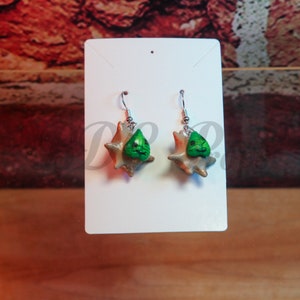 Puede incluir: Un par de pendientes con un diseño de hoja verde y marrón. Los pendientes están en una tarjeta blanca.