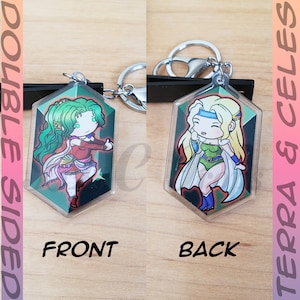 May include: Double-sided keychain featuring a green-haired character with a red and white outfit on one side and a blonde-haired character with a green and white outfit on the other side. The keychain is shaped like a hexagon with rounded edges.