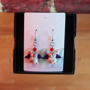 May include: A pair of silver dangle earrings featuring white bat-shaped charms with red noses and purple wings.