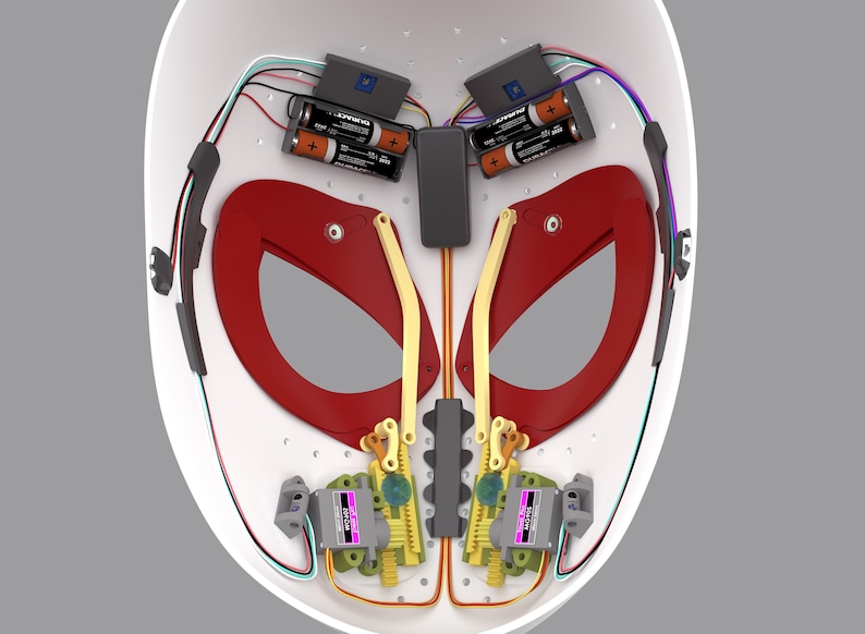 K&ouml;nnte beinhalten: Eine wei&szlig;e Maske mit roten und goldenen Akzenten. Das Innere der Maske ist sichtbar und zeigt ein komplexes System aus Zahnr&auml;dern, Dr&auml;hten und Batterien. Die Maske ist so konzipiert, dass sie sich bewegt und &ouml;ffnet und schlie&szlig;t.