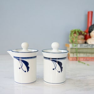 May include: A set of two white ceramic creamer and sugar containers with blue floral designs and lids.