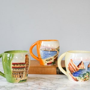 Puede incluir: Tres tazas de cerámica con escenas pintadas de ciudades italianas. Las tazas son verdes, naranjas y blancas con los nombres "Pisa", "Capri" y "Cinque Terre" escritos en la parte inferior.