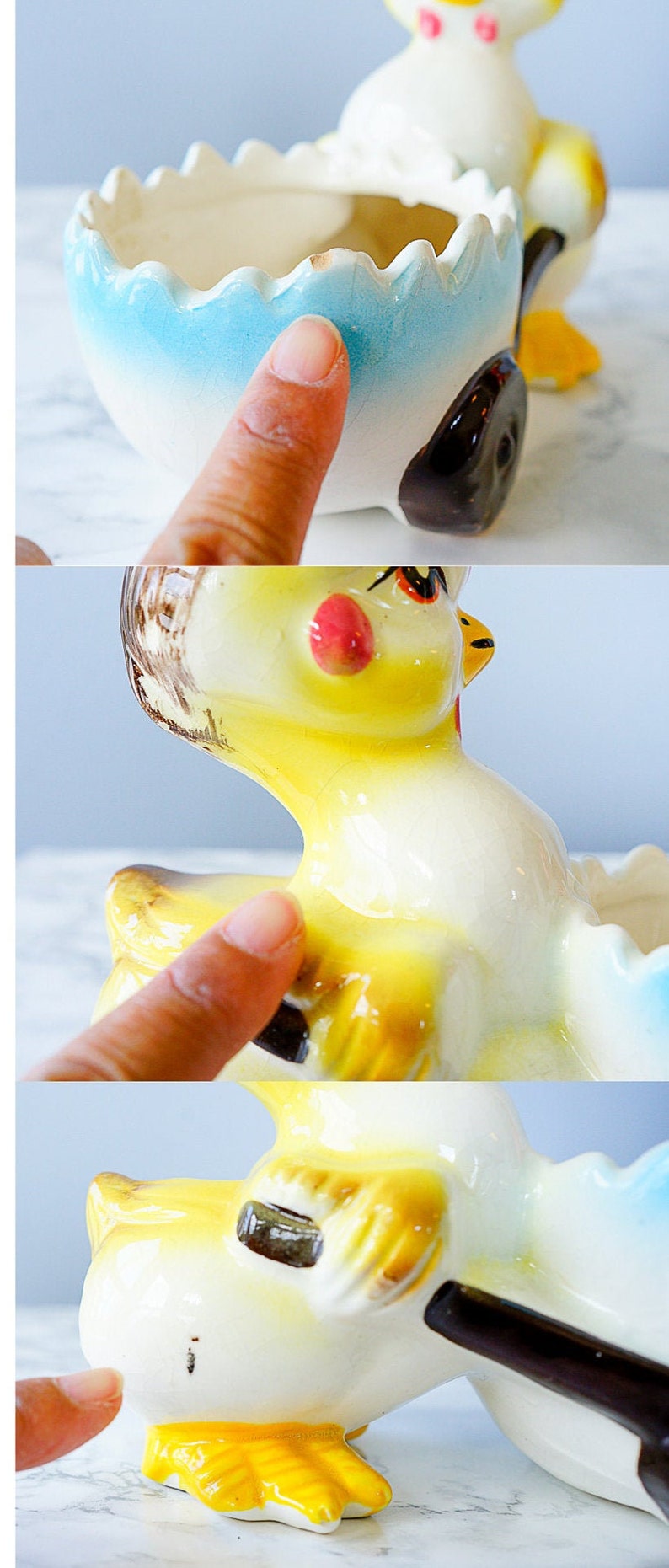 May include: A yellow ceramic chick pushing a blue and white egg-shaped planter. The chick has a brown beak, black eyes, and a pink blush on its cheeks. The planter has a scalloped edge.